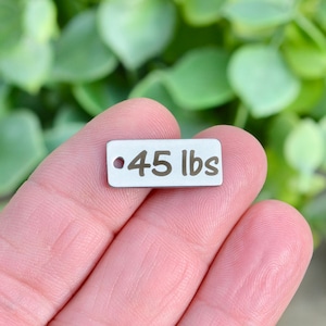 May include: A silver metal tag with a hole at the top and the text "45 lbs" engraved in gold.