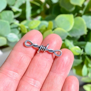 May include: Silver-toned charm shaped like barbed wire, with a looped design at each end.
