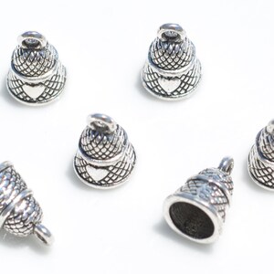 Peut inclure: Un ensemble de six breloques en forme de cloche en m&eacute;tal argent&eacute;, chacune pr&eacute;sentant un motif quadrill&eacute; textur&eacute; sur la partie sup&eacute;rieure et un d&eacute;tail en forme de c&oelig;ur lisse sur le bord inf&eacute;rieur, avec une petite boucle de fixation au sommet.