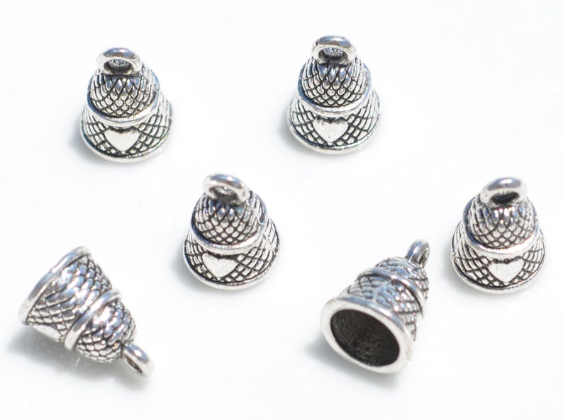 Peut inclure: Un ensemble de six breloques en forme de cloche en m&eacute;tal argent&eacute;, chacune pr&eacute;sentant un motif quadrill&eacute; textur&eacute; sur la partie sup&eacute;rieure et un d&eacute;tail en forme de c&oelig;ur lisse sur le bord inf&eacute;rieur, avec une petite boucle de fixation au sommet.