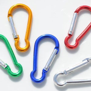 May include: Five colorful metal carabiners in different colors: orange, green, blue, red, and silver. The carabiners are all closed and are lying on a white surface.