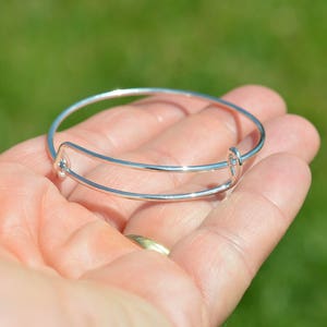 May include: A silver expandable bangle bracelet with a simple design.