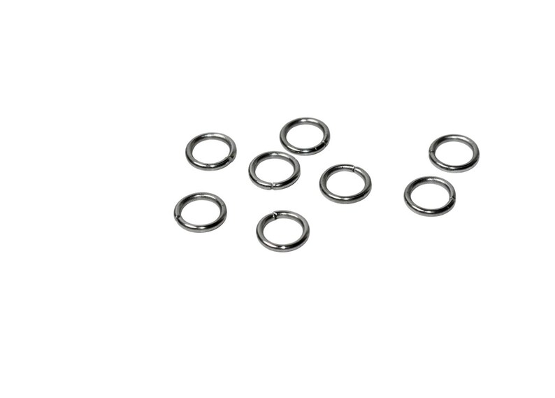May include: A collection of seven small, circular metal jump rings with a smooth, polished silver-tone finish. Each ring features a single, thin cut along its circumference, allowing the ring to be opened and closed for connecting jewelry components.