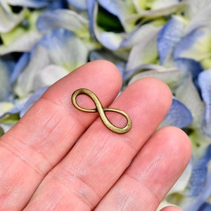 May include: A gold infinity symbol charm, held in a hand against a background of blue and white flowers.