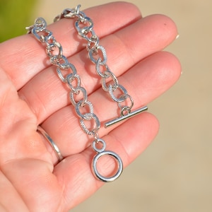 May include: A silver chain necklace with a toggle clasp and a circular pendant.