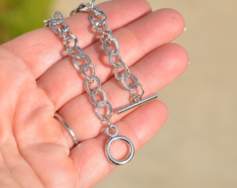 May include: A silver chain necklace with a toggle clasp and a circular pendant.