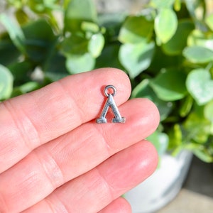 May include: Silver charm in the shape of the Greek letter Delta. The charm has a loop at the top for attaching to a necklace or bracelet.