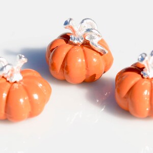 May include: Three small orange ceramic pumpkins with silver stems. The pumpkins are about 1 inch in diameter.