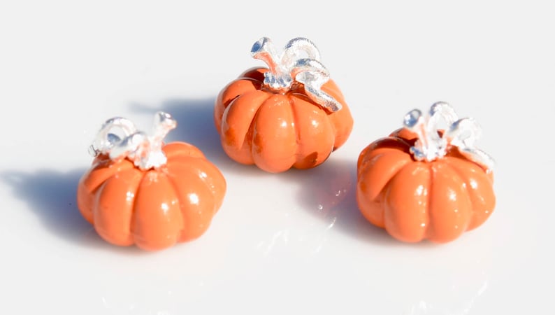 May include: Three small orange ceramic pumpkins with silver stems. The pumpkins are about 1 inch in diameter.