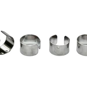 May include: Four silver metal rings with a small hole in each. The rings are open on one side and have a slightly curved shape.