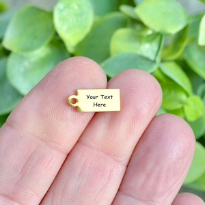 May include: A gold-coloured metal tag with a hole for a string or chain. The tag is rectangular and has the text "Your Text Here" engraved on it.
