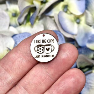 Peut inclure: Un petit médaillon rond en métal blanc orné d'un motif noir représentant deux tasses, l'une à pois et l'autre avec un cœur, accompagné du texte noir "I LIKE BIG CUPS...AND I CANNOT LIE!" avec un petit trou en haut pour la fixation.