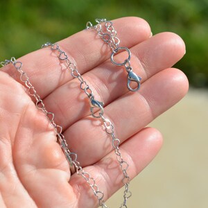 May include: A silver heart-shaped chain necklace with a lobster clasp closure.