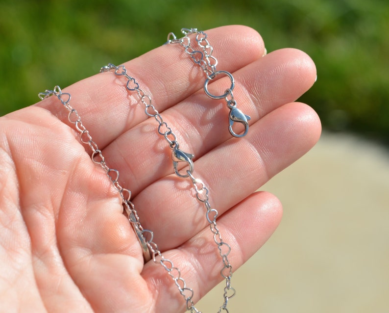 May include: A silver heart-shaped chain necklace with a lobster clasp closure.