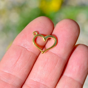 May include: A gold-colored heart-shaped pendant with a loop at the top for attaching to a chain or cord.