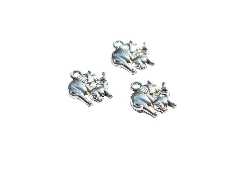 May include: Three silver charms in the shape of elephants. Each charm features a larger elephant carrying a smaller elephant on its back.