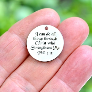 May include: A round, silver-colored pendant with a small hole at the top. The pendant features the engraved text: "I can do all things through Christ who Strengthens Me Phil. 4:13". The background is a soft green.