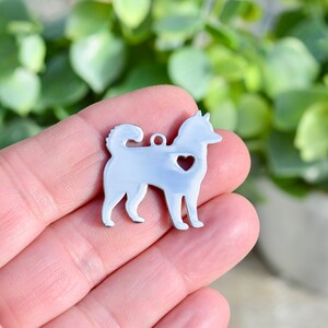 Puede incluir: Encanto de metal plateado con forma de perro con un coraz&oacute;n recortado en el pecho. El encanto se sostiene en la mano de una persona.