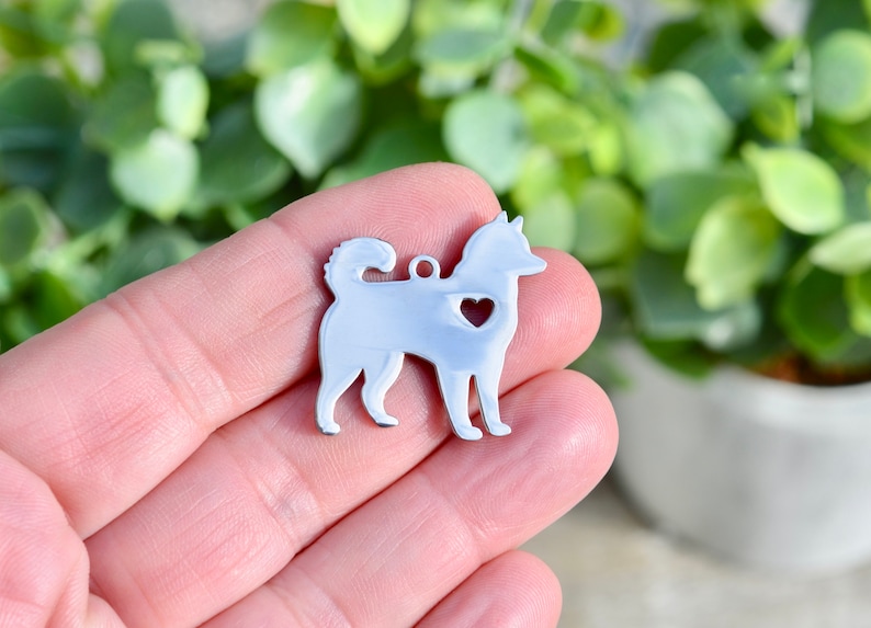 Puede incluir: Encanto de metal plateado con forma de perro con un coraz&oacute;n recortado en el pecho. El encanto se sostiene en la mano de una persona.