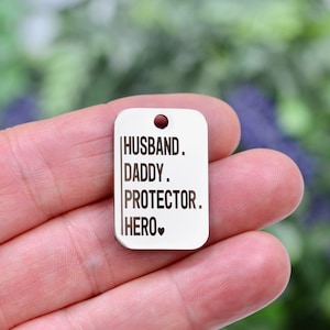 May include: Silver metal tag with the words "Husband. Daddy. Protector. Hero." and a small heart symbol.