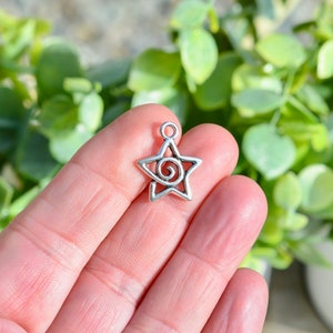 May include: Silver-toned metal star charm with a spiral design. The charm is approximately 2.5 cm in size and has a loop at the top for attaching to jewellery or other crafts.
