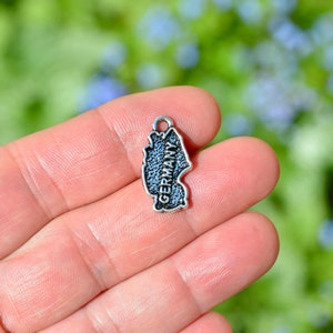 May include: Silver charm shaped like the outline of Germany with the word "Germany" inscribed on it.
