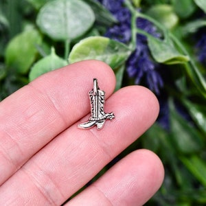 May include: Silver charm in the shape of a cowboy boot with a spur. The boot has a detailed design and is a great addition to any jewelry collection.