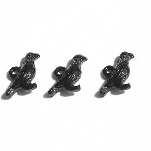 May include: Three black metal crow charms with a loop for attaching to a necklace, bracelet, or other jewellery.