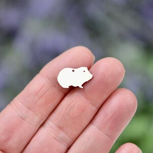 May include: A white metal charm shaped like a guinea pig. The charm has two small holes for attaching to a necklace or bracelet.