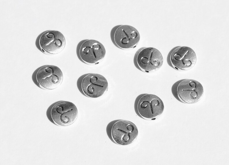 May include: A collection of silver-toned metal beads with the astrological symbol for Aries engraved on each bead.