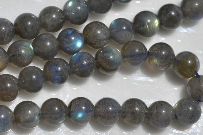 Op de afbeelding: Een streng ronde, donkergrijze labradorit kralen met iriserende blauwe en groene flitsen.