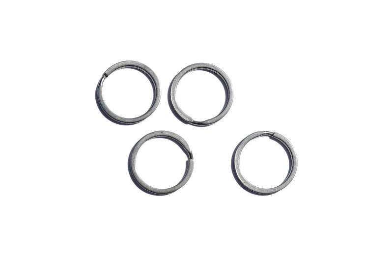 May include: Five silver key rings, all the same size and shape, are arranged in a triangular pattern on a white background.
