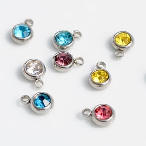 May include: Assortment of small, round, colorful crystal charms with silver metal loops. The charms are in shades of blue, yellow, pink, and clear.