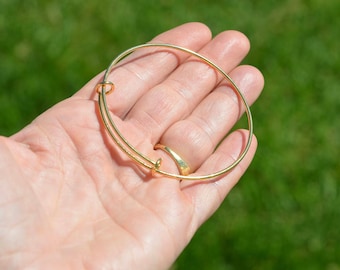 May include: A gold-toned bangle bracelet with a simple, circular design. The bracelet is open and has a spring clasp.