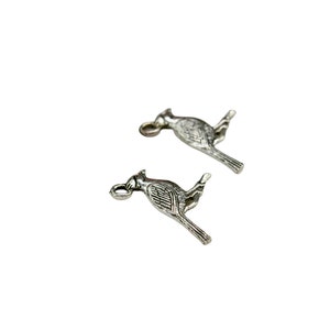 K&ouml;nnte beinhalten: Zwei silberne Vogel-Anh&auml;nger aus Metall mit einer &Ouml;se zum Anbringen an einer Halskette oder einem Armband.