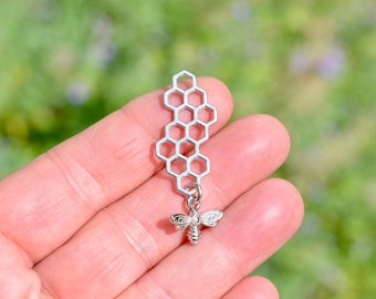 May include: Silver charm featuring a honeycomb design with a small bee pendant.