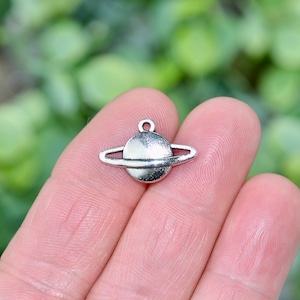 May include: A silver charm shaped like a planet with rings. The charm is small and detailed, and would be ideal for adding to a necklace or bracelet.