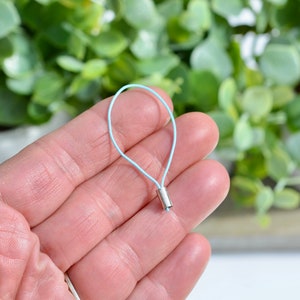 Peut inclure: Un cordon élastique bleu clair avec un bouton en métal argenté. Le cordon est tenu dans une main.