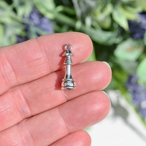 May include: Silver chess piece charm in the shape of a king. The charm is detailed with a pointed top and a round base.