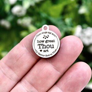 May include: A circular silver-toned metal charm featuring the engraved text "Then sings my soul, how great Thou art, my Savior God to Thee" with musical notes and a small heart symbol. The charm includes a small loop at the top for attachment.