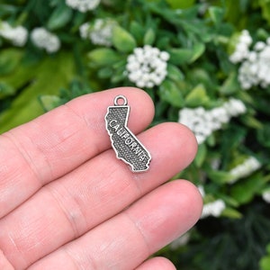 May include: Silver charm shaped like the state of California with the word "CALIFORNIA" inscribed on it.