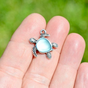 May include: Silver turtle charm with a white iridescent shell. The charm is perfect for jewelry making or adding a touch of whimsy to crafts.