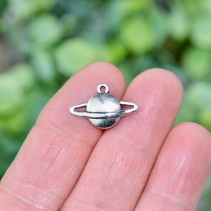 May include: A silver charm in the shape of a planet with rings. The charm is small and detailed, and would be perfect for adding to a necklace or bracelet.
