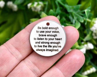 May include: A circular silver-toned metal charm featuring an engraved message that reads: Be bold enough to use your voice, brave enough to listen to your heart and strong enough to live the life you've always imagined. The charm has a small hole.