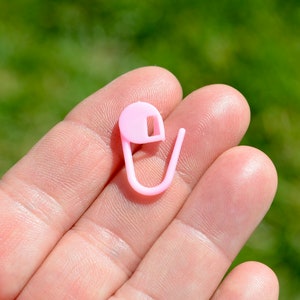 May include: A pink plastic safety pin with a rounded head and a hook closure.