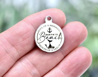 May include: A circular silver-toned metal charm featuring an engraved anchor, a mermaid tail, and the text "SOUL OF A MERMAID, MADE FOR THE BEACH, MOUTH OF A SAILOR" arranged in a circular pattern around the center design with a small loop at the top.