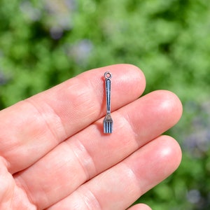 May include: Silver charm in the shape of a fork. The charm is small and detailed, with a smooth, shiny finish.