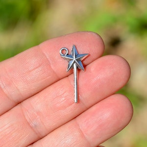 May include: Silver charm in the shape of a star on a stick. The charm has a loop at the top for attaching to a necklace or bracelet.