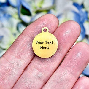 May include: A gold-colored round metal tag with a hole at the top for attaching to a chain or string. The tag has the text "Your Text Here" engraved on it.