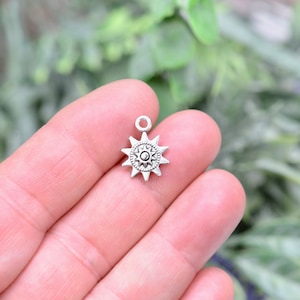 Peut inclure: Breloque en argent avec un motif en étoile. L'étoile a un petit cercle au centre et est entourée de huit pointes.